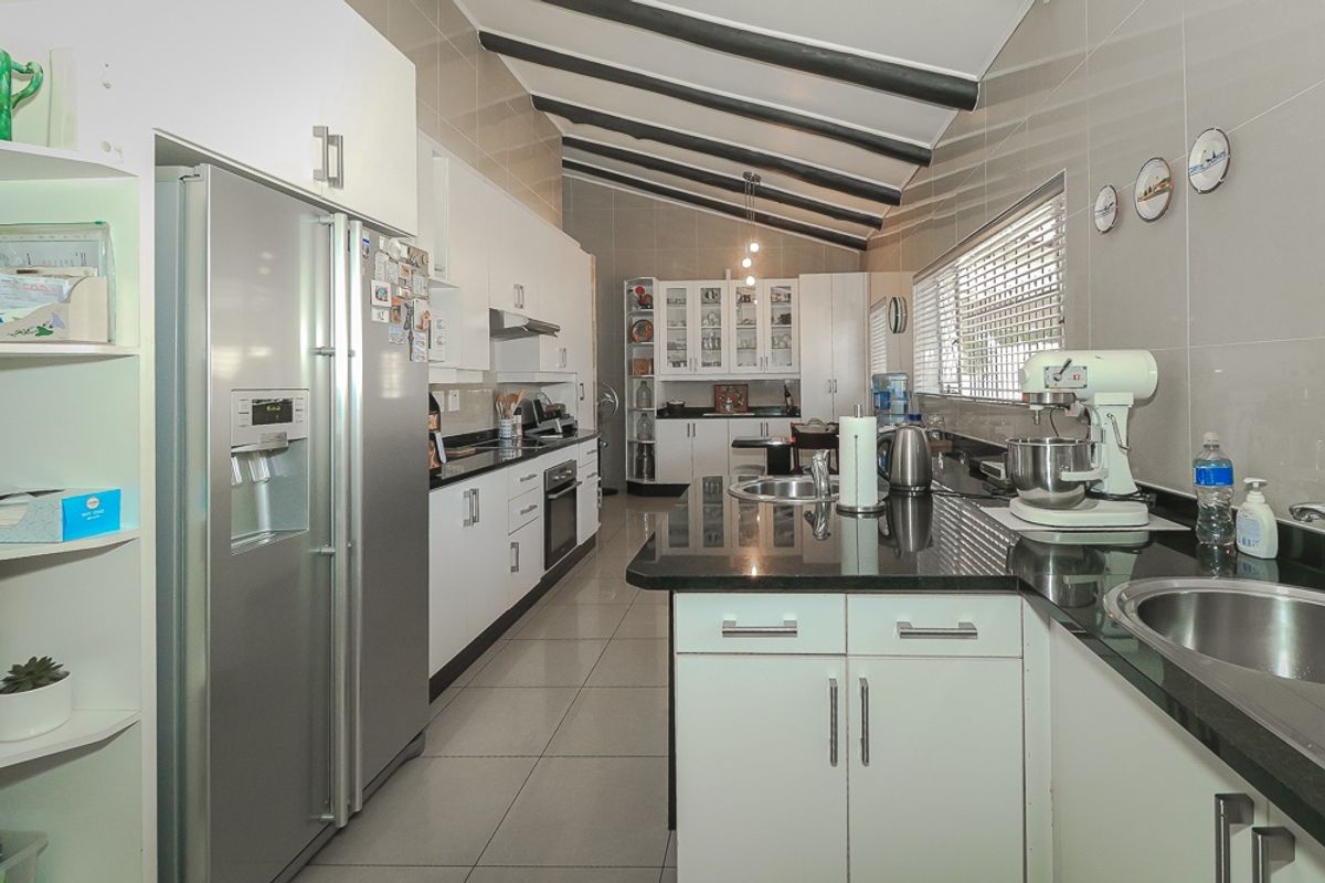 A well-appointed kitchen featuring white cabinetry, dark granite countertops, tiled splashbacks, and exposed ceiling beams, offering a functional and modern workspace.