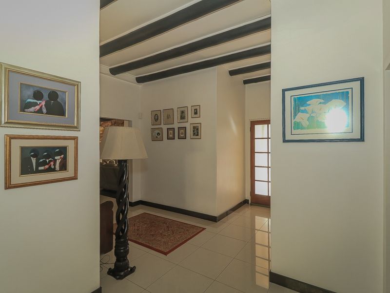 A bright hallway featuring tiled flooring and exposed dark timber ceiling beams, leading towards a glass-paneled exterior door.