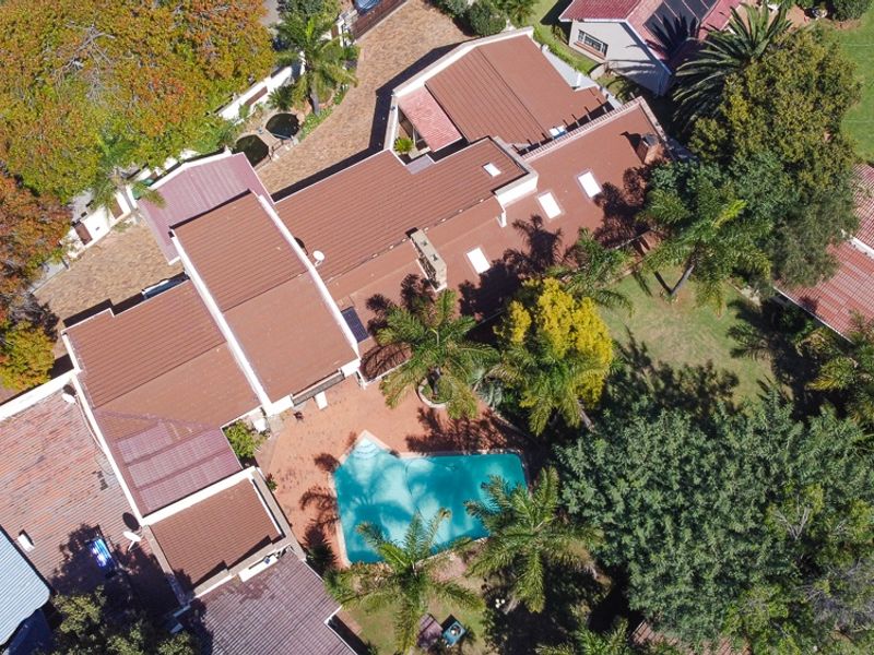 Aerial view of the property showcasing the expansive roof structure, swimming pool, paved patio area, and established garden surroundings.