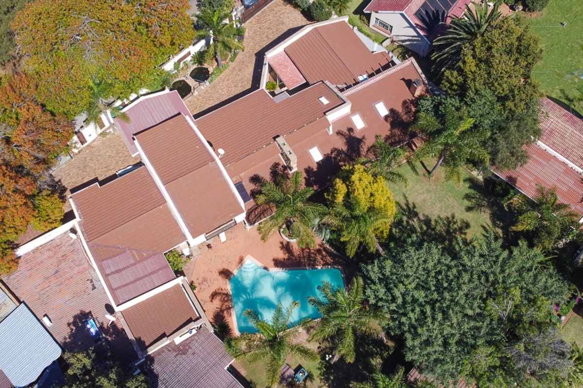 Aerial view of the property showcasing the expansive roof structure, swimming pool, paved patio area, and established garden surroundings.