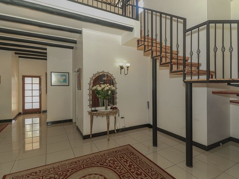 Spacious entrance hall featuring exposed timber ceiling beams, tiled flooring, and a distinctive open-tread staircase with wrought iron balustrades.