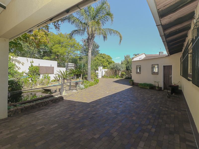 A spacious paved rear courtyard featuring a covered patio area, a small pond, and secure perimeter walling with electric fencing.