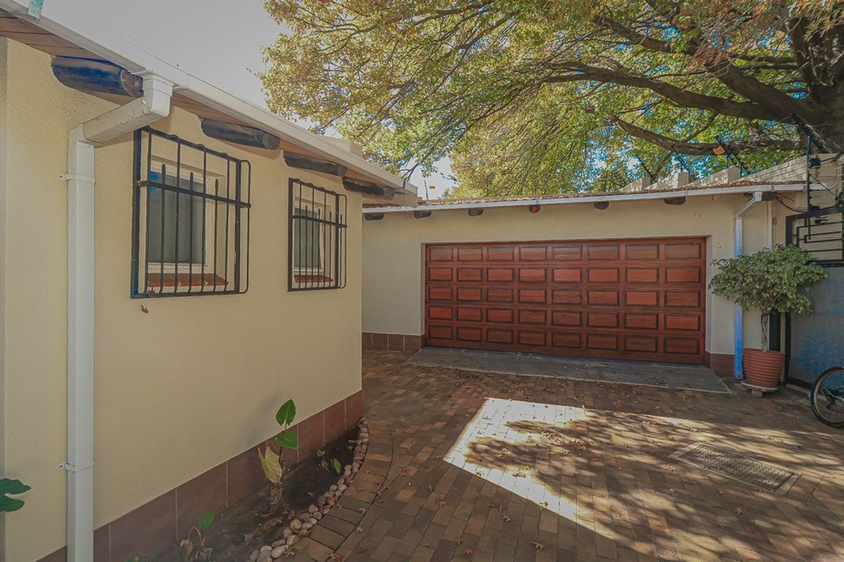 A well-maintained rear exterior area featuring a brick-paved driveway, a wooden garage door, and windows fitted with security bars.