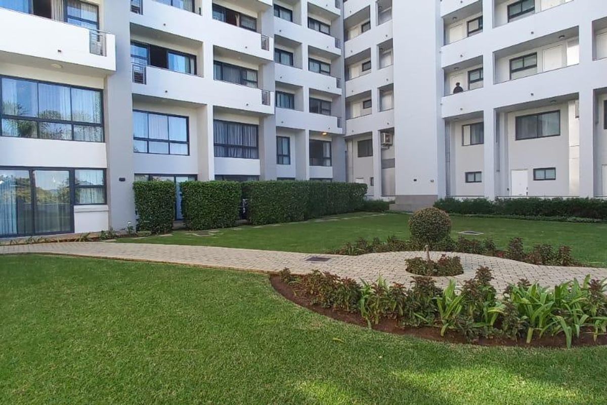 A well-maintained communal garden area featuring paved walkways, manicured lawns, and landscaped shrubbery set within a modern apartment complex.