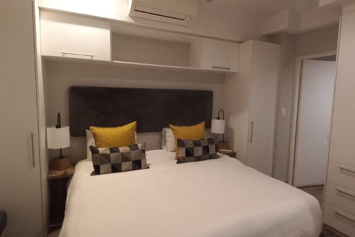 A well-appointed bedroom featuring extensive built-in cabinetry, overhead storage, and a wall-mounted air conditioning unit for climate control.
