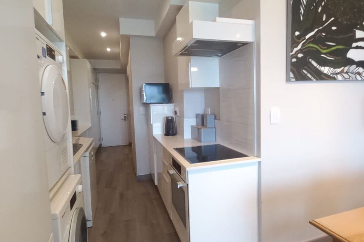 Compact modern kitchen featuring built-in cabinetry, integrated oven, electric hob, extractor fan, and laundry appliances, finished with clean lines and neutral tones.