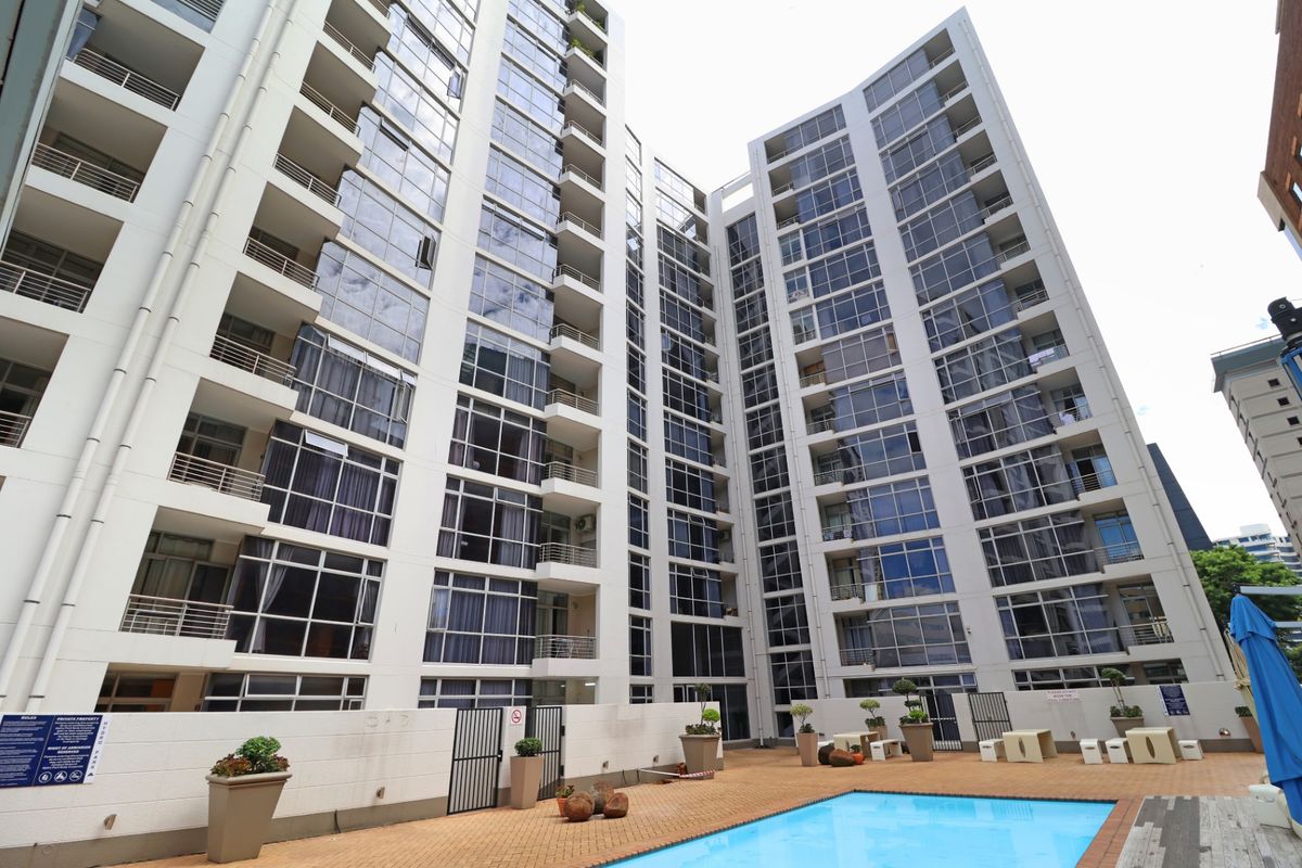 A view of the apartment building facade featuring a swimming pool area with paved decking and integrated balconies.