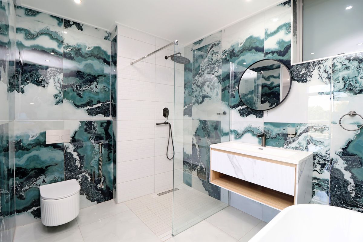 Modern bathroom featuring striking teal and white marble-effect wall tiles, a walk-in glass shower, wall-mounted toilet, and a contemporary floating vanity unit.