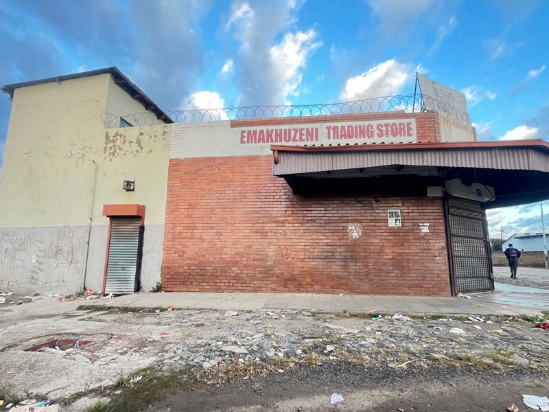 Commercial storefront featuring brick facade, metal security shutters, and protective razor wire, showing signs of significant wear and exterior damage.