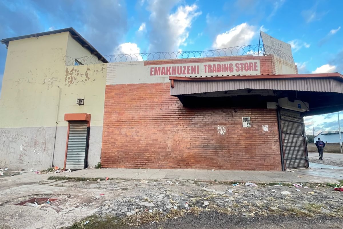 Commercial storefront featuring brick facade, metal security shutters, and protective razor wire, showing signs of significant wear and exterior damage.