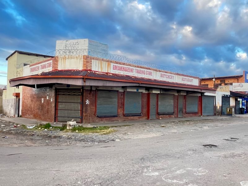 Commercial corner property featuring a brick facade, metal security shutters, and perimeter razor wire, currently showing significant signs of wear and weathering.