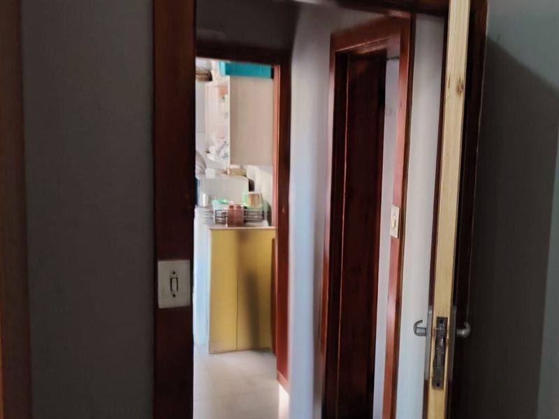 A narrow hallway featuring timber door frames and tiled flooring, leading towards a kitchen area.