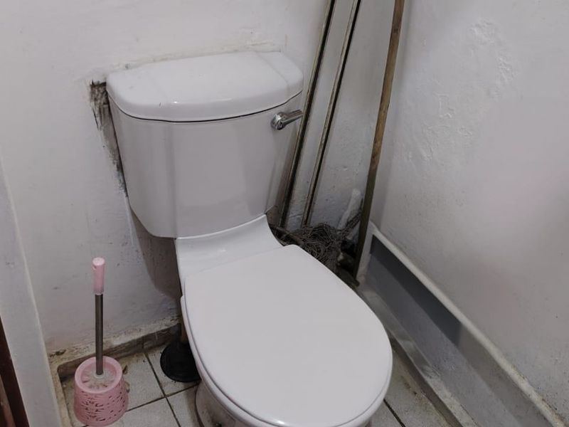 A small bathroom featuring a standard toilet and tiled flooring, currently showing signs of wear and requiring maintenance to the wall and floor finishes.