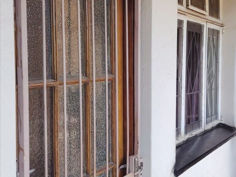 Exterior view of an apartment entrance featuring a timber door with a security gate and leaded glass windows on a concrete porch.