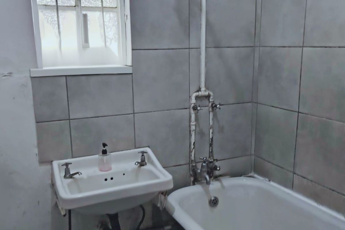 A dated bathroom featuring a wall-mounted basin, bathtub, and exposed plumbing, requiring cosmetic updates and repairs to the wall finishes.
