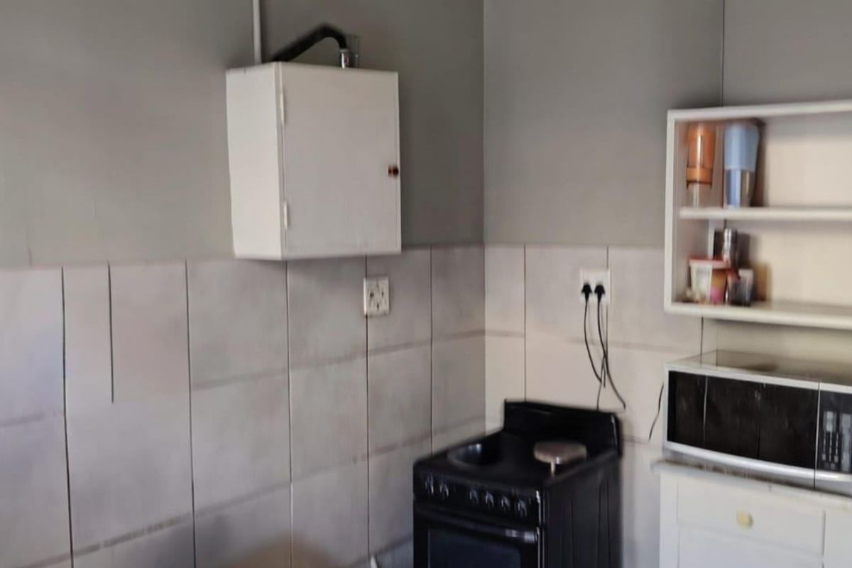 A compact kitchen area featuring a tiled splashback, wall-mounted storage, and a freestanding electric stove with basic utility finishes.