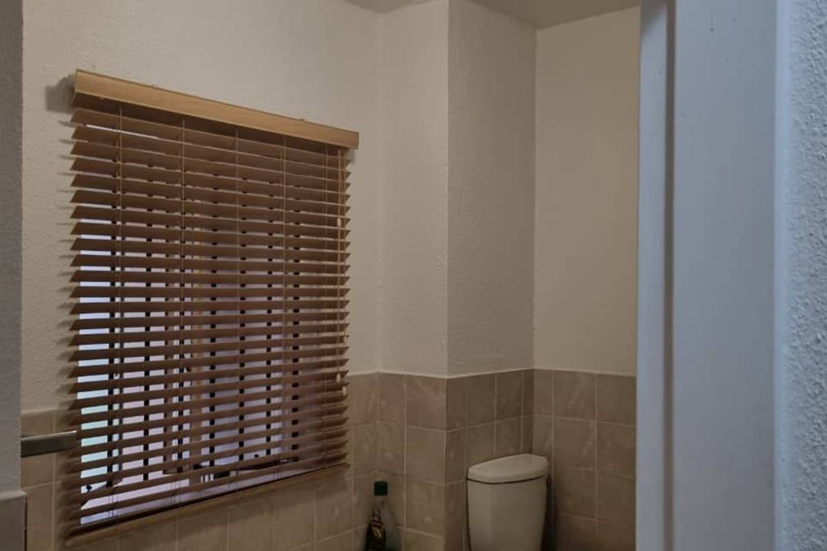 A functional bathroom featuring a built-in bathtub with tiled surround, a standard toilet, and wooden venetian blinds.