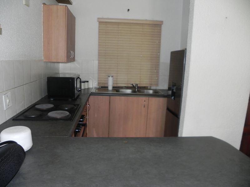 Compact kitchen featuring laminate countertops, built-in electric hob, double sink, and wooden cabinetry with neutral wall tiles.