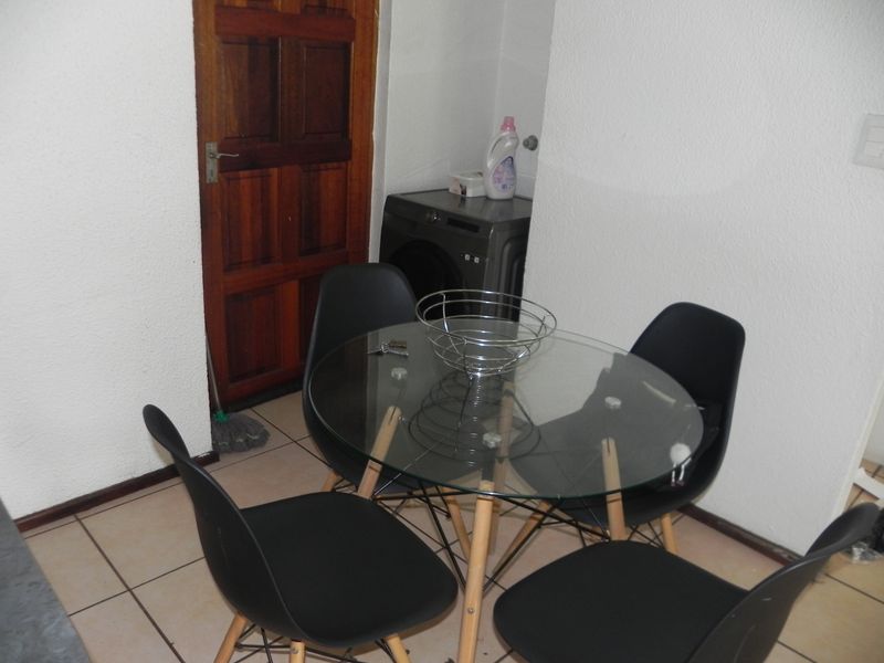 A functional dining area featuring tiled flooring and a wooden door, with a dedicated laundry nook containing a washing machine.