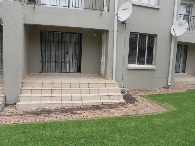 Ground floor apartment exterior featuring a tiled patio area, security gate, and direct access to a shared garden space.