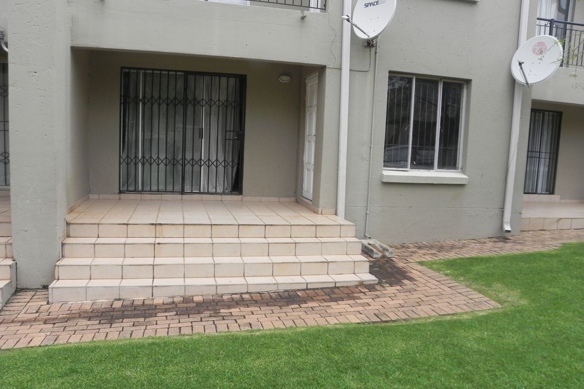 Ground floor apartment exterior featuring a tiled patio area, security gate, and direct access to a shared garden space.