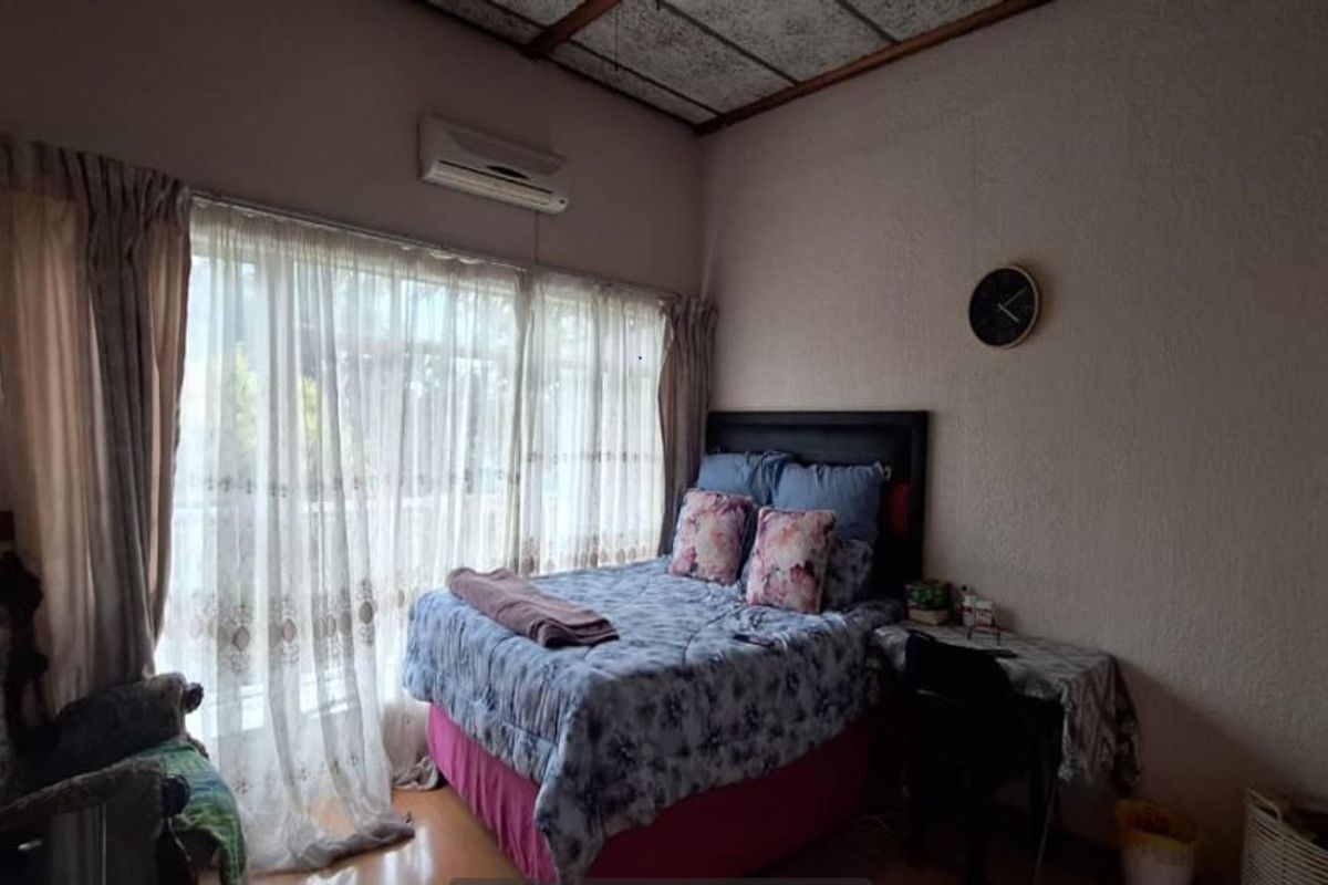 A bedroom featuring laminate flooring, a split-system air conditioner, and a textured ceiling, offering a functional space with potential for cosmetic updates.