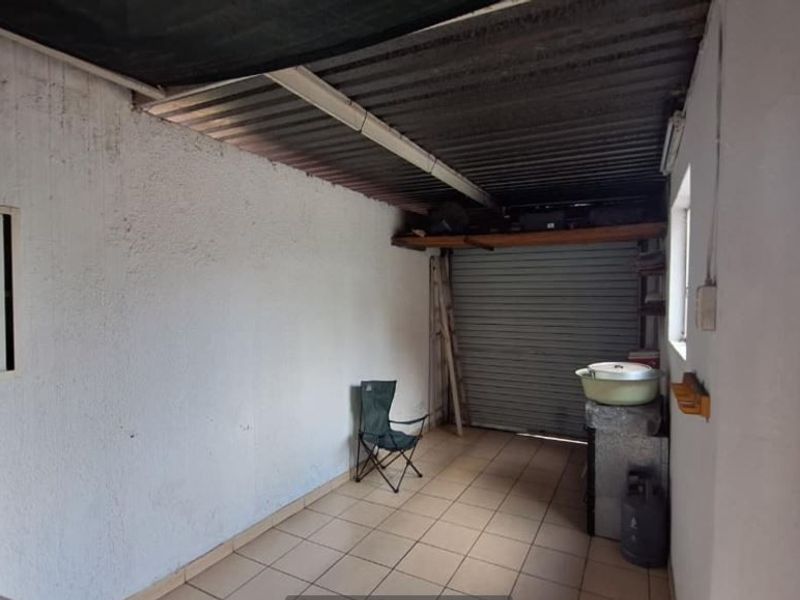 A functional garage space featuring tiled flooring, a roller shutter door, and corrugated metal roofing, offering potential for storage or workshop use.