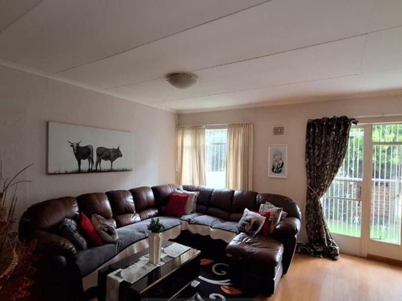 A comfortable living room featuring laminate flooring, a ceiling light fixture, and a glass sliding door with a security gate leading to the garden.