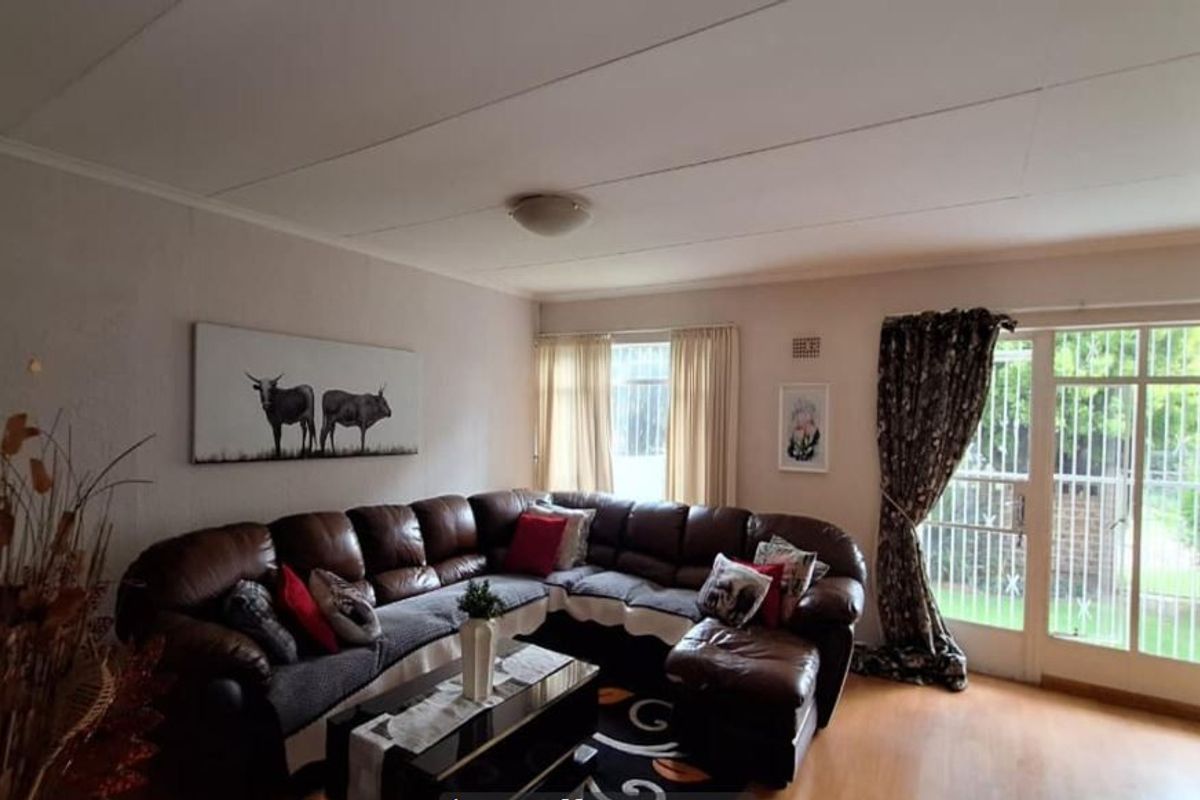 A comfortable living room featuring laminate flooring, a ceiling light fixture, and a glass sliding door with a security gate leading to the garden.