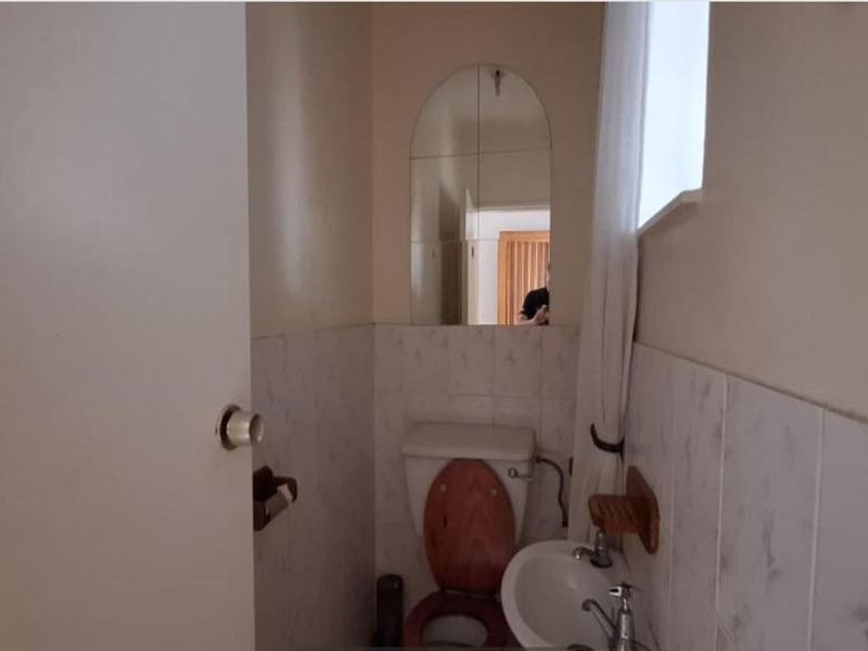 A compact guest bathroom featuring a wall-mounted basin, toilet, and tiled wall finishes with an arched mirror.