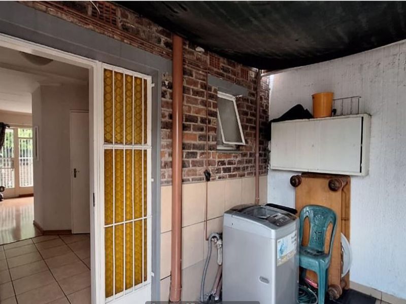 Covered outdoor laundry area featuring exposed brick walls, tiled flooring, and direct access to the interior living space.