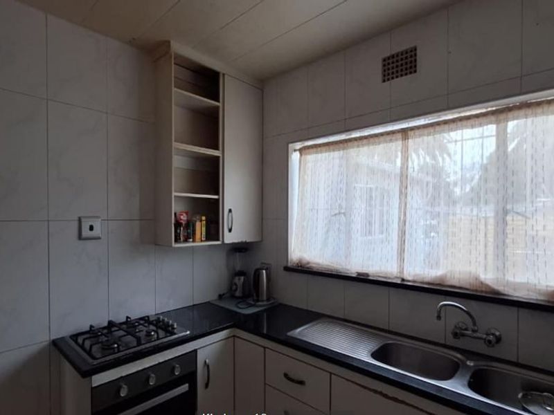 A functional kitchen featuring granite countertops, a gas hob, built-in oven, and double basin sink with ample storage cabinetry.