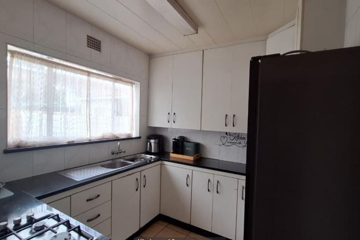 A functional kitchen featuring white cabinetry, dark granite countertops, a gas hob, and a tiled splashback with a window for natural light.