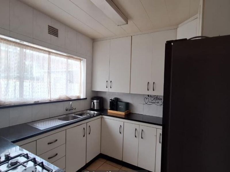 A functional kitchen featuring white cabinetry, dark granite countertops, a gas hob, and a tiled splashback with a window for natural light.