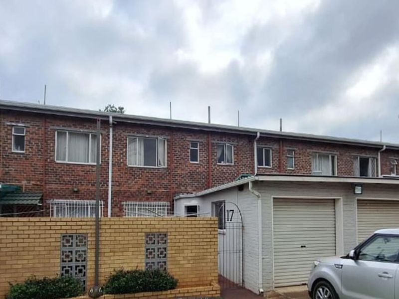 Front elevation of a face-brick townhouse complex featuring roller garage doors, security gates, and a low brick boundary wall with breeze block accents.