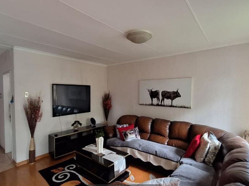 A comfortable living room featuring a mix of tiled and laminate flooring, neutral walls, and direct access to an adjacent hallway.