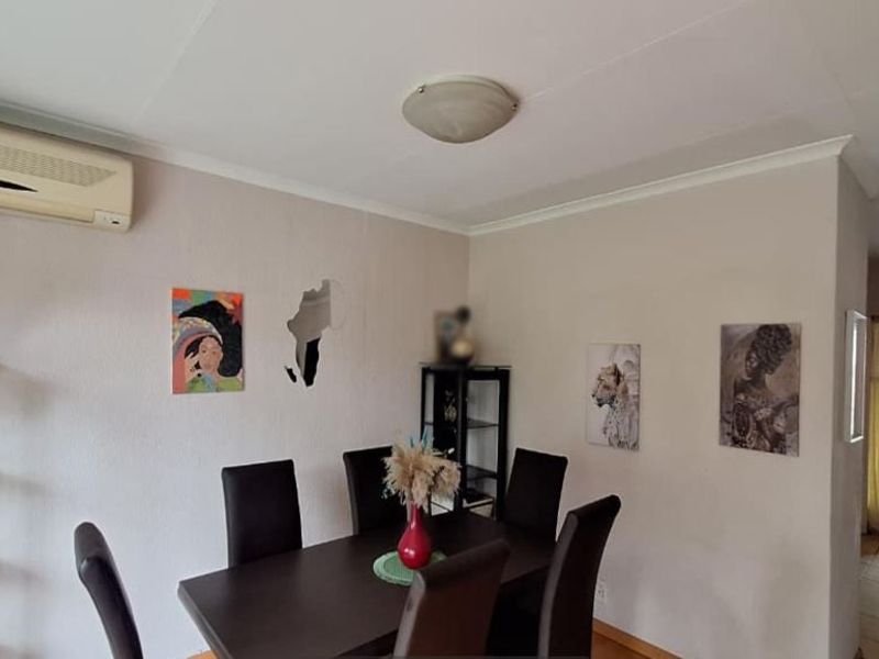 A dining area featuring tiled flooring, a wall-mounted air conditioning unit, and access to an adjacent hallway.