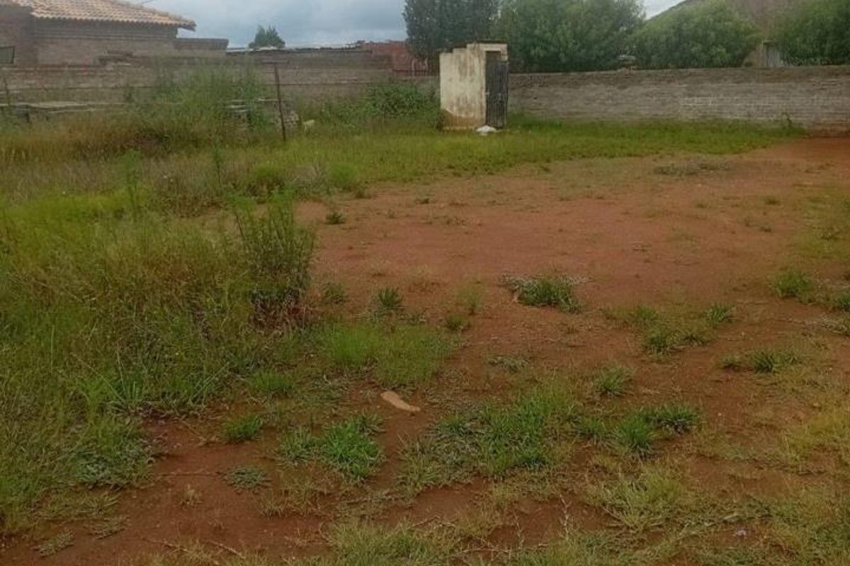 A vacant residential plot featuring a perimeter wall and a small, weathered utility structure on the property.
