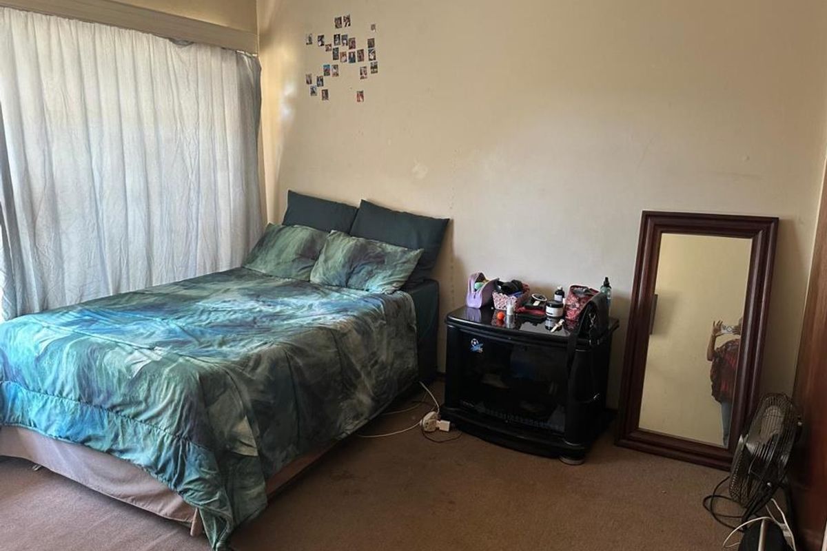A bedroom featuring carpeted flooring and a large window with curtains, providing a functional space ready for cosmetic updates.