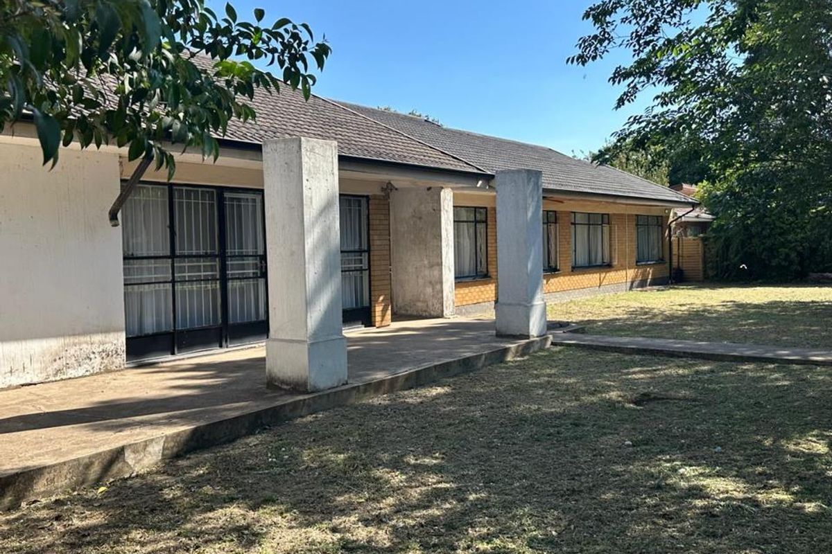 Rear view of the house featuring a concrete patio, brick facade, and tiled roof, set against a large garden area.