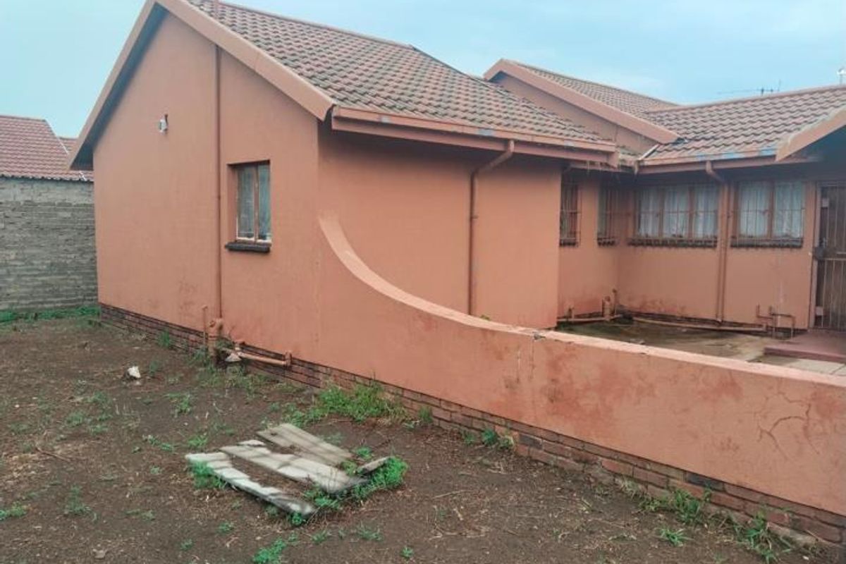 Rear view of the property showing the exterior brick walls, tiled roof, and a small yard area with a low boundary wall.