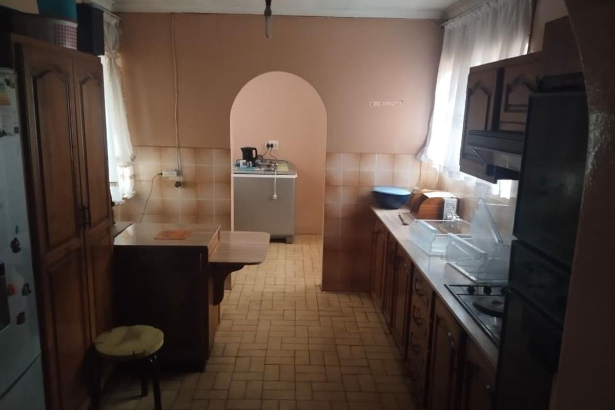 A dated kitchen featuring wooden cabinetry, tiled backsplash, and a functional layout with an adjoining archway leading to a secondary utility area.