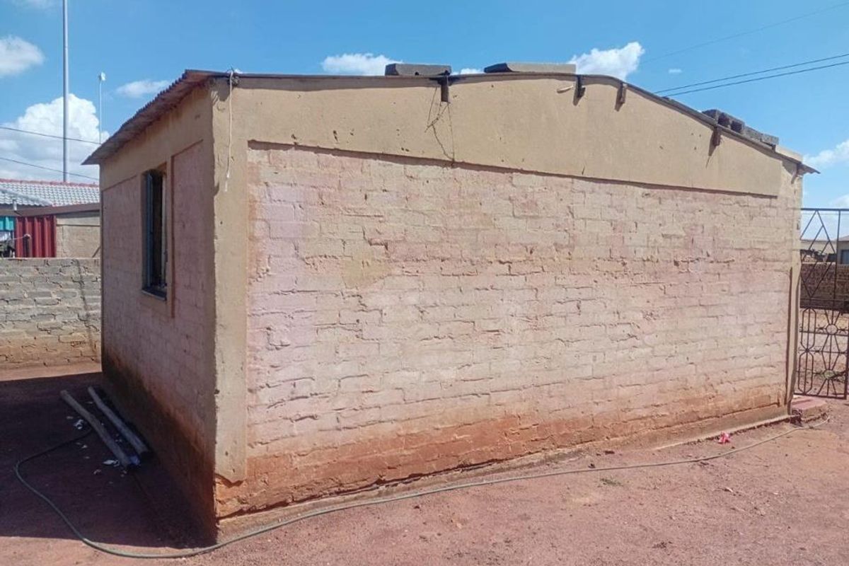 Rear view of a small outbuilding featuring exposed brick walls and a corrugated metal roof, showing significant signs of wear and unfinished exterior surfaces.