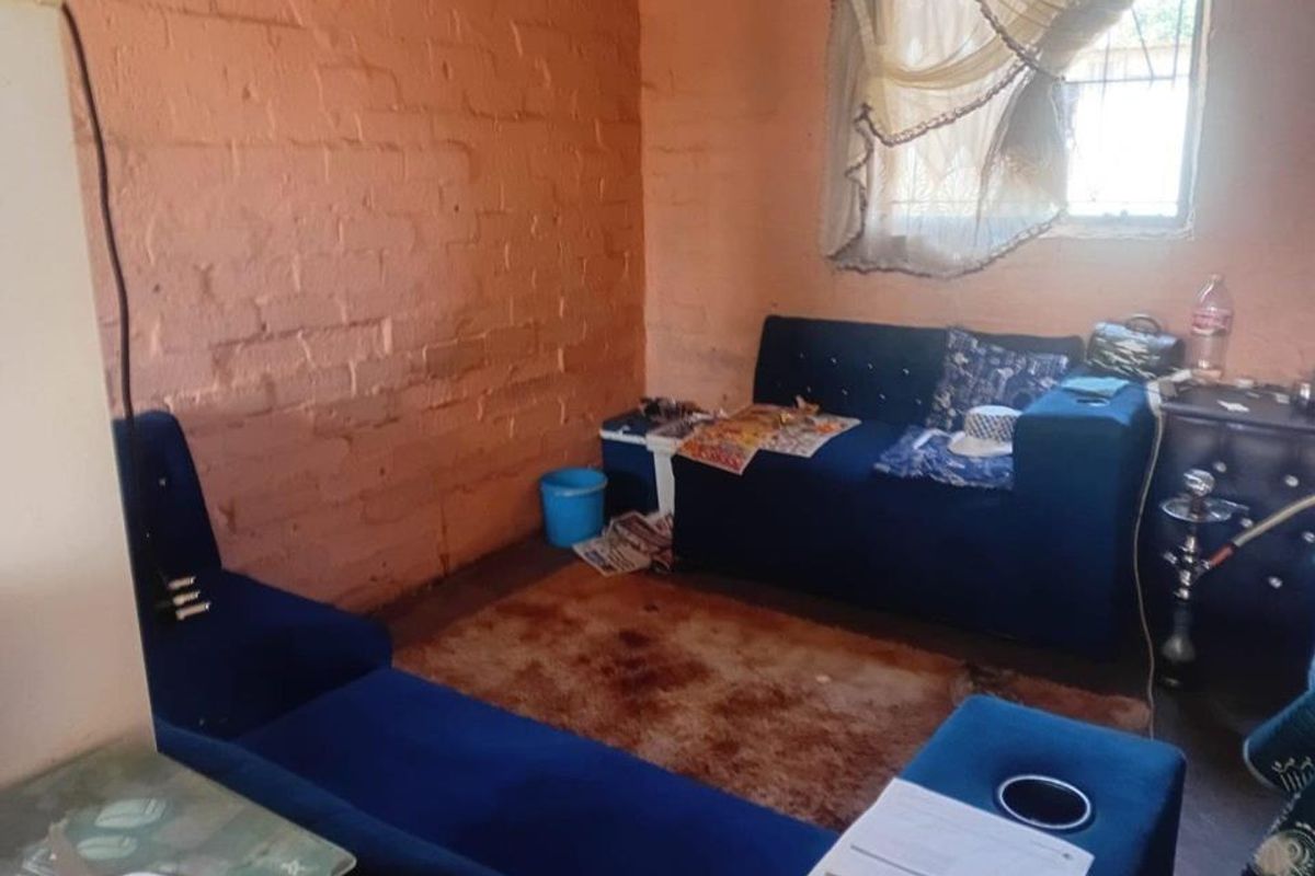 A living room featuring exposed brick walls and a window with security bars, requiring cosmetic updates to improve the interior finish.