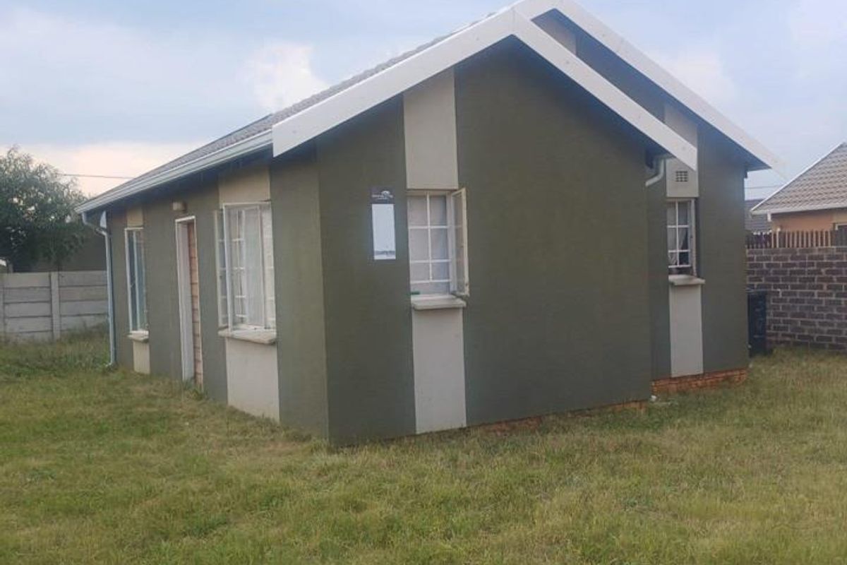 A view of the rear exterior of a detached house featuring plastered walls, a tiled roof, and steel window frames set on a grassed plot.