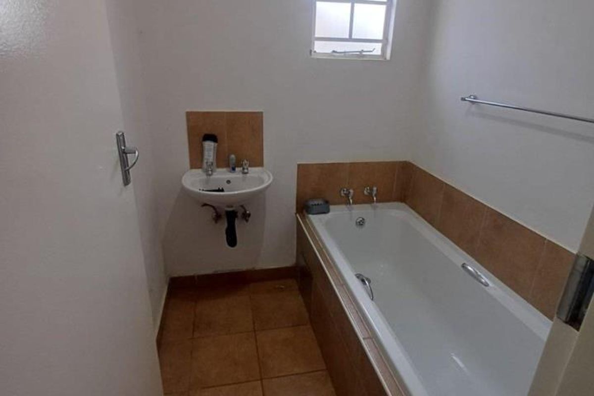 A functional bathroom featuring a bathtub, wall-mounted basin, and tiled finishes, offering a clean space ready for potential modern updates.