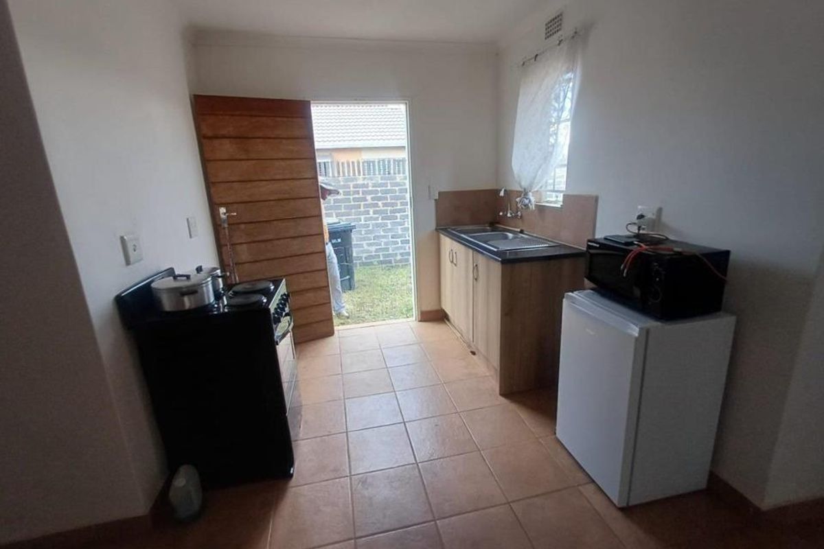A functional kitchen area featuring tiled flooring, basic cabinetry with a stainless steel sink, and direct access to the rear exterior.