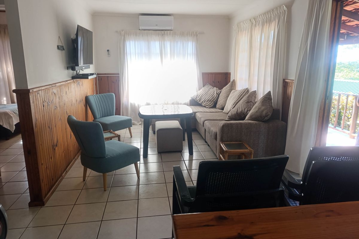 A living room featuring timber wall paneling, tiled flooring, a ceiling fan, and a split system air conditioner with access to an outdoor area.