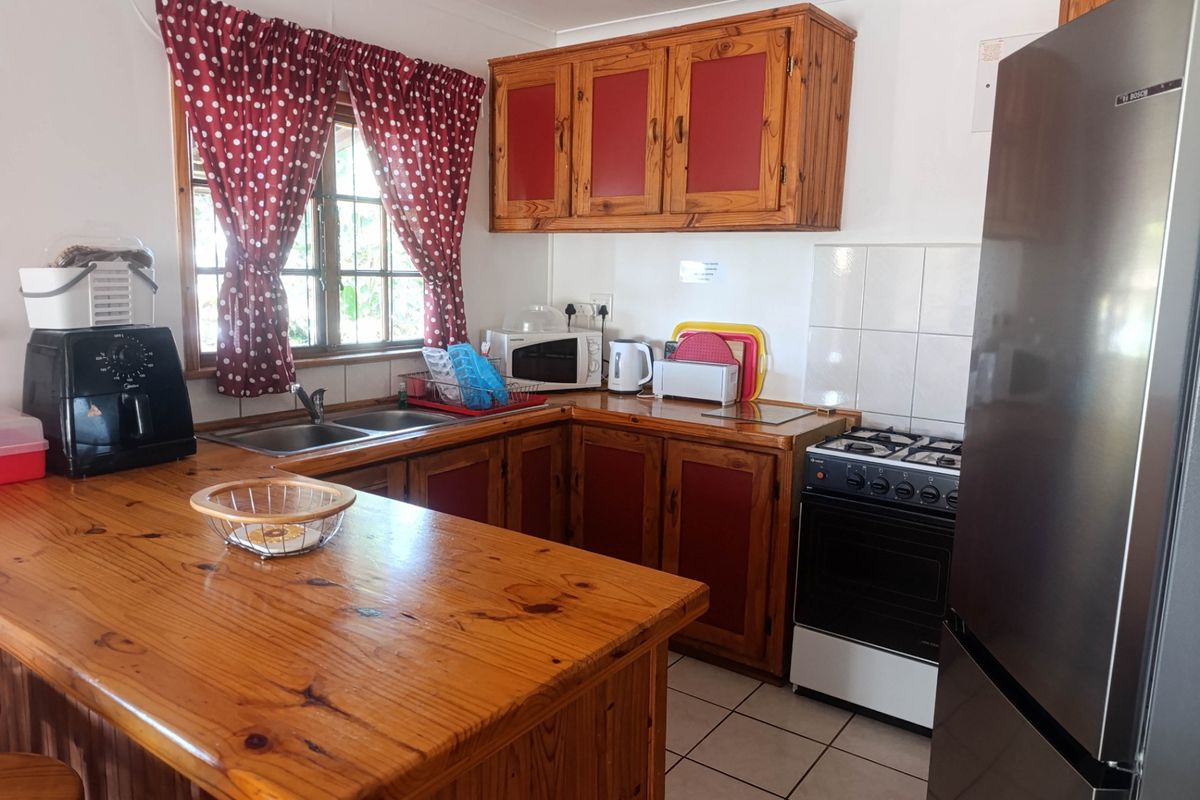 A functional kitchen featuring wooden cabinetry, a double basin sink, tiled splashback, and a freestanding gas stove with tiled flooring.
