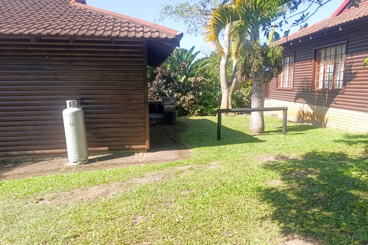 Rear exterior view of the property featuring timber log cladding, a tiled roof, and a paved area with a built-in braai.